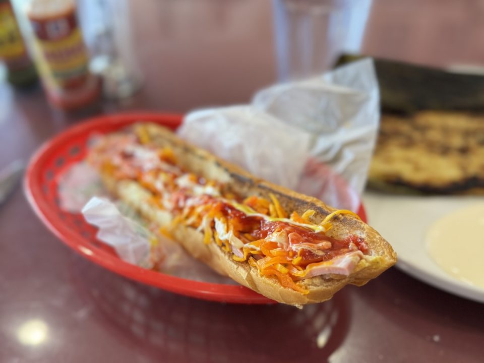 A long, thin sandwich in a red plastic basket with deli paper