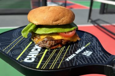 A cheeseburger served on top of a pickleball paddle.