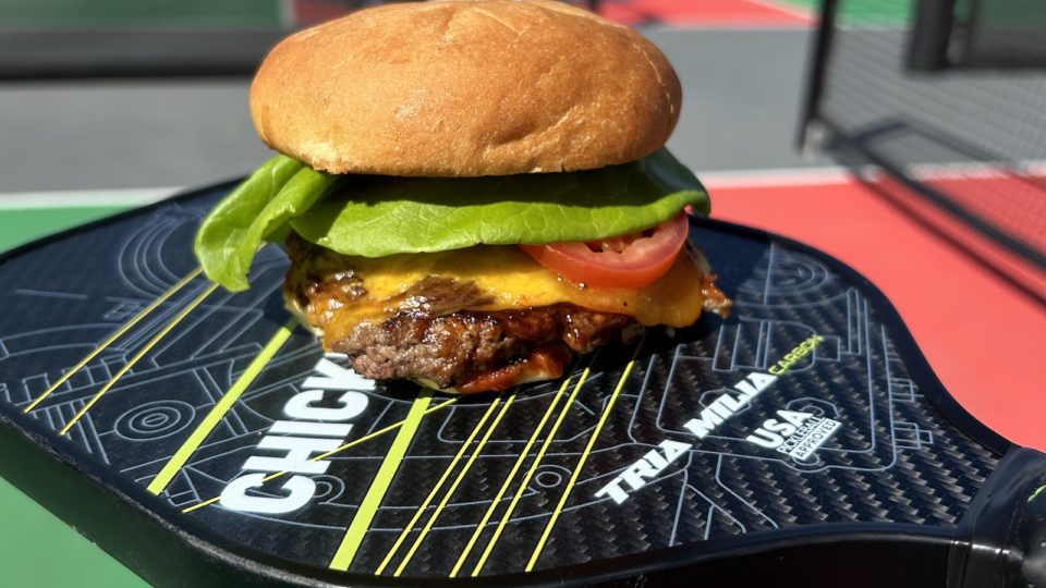 A cheeseburger served on top of a pickleball paddle.