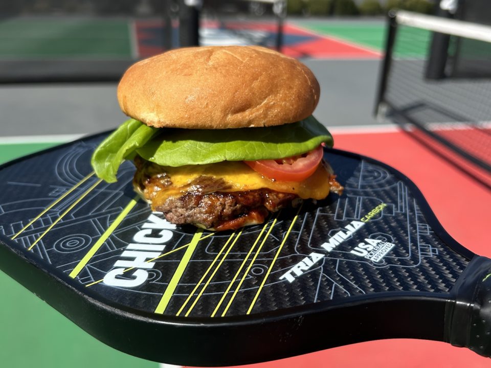 A cheeseburger served on top of a pickleball paddle.