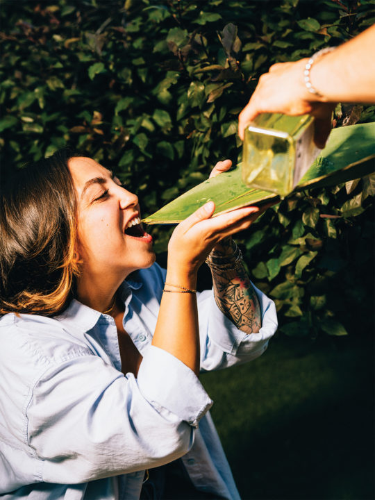 A woman drinks mezcal from an agave leaf