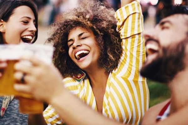 Two women and a man laughing while they cheers each other.