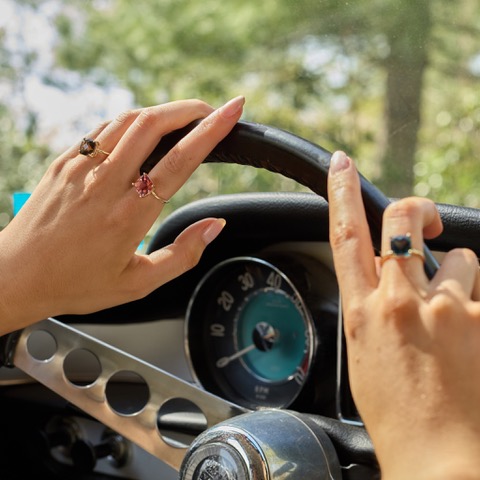 A woman's hands on a car steering wheel wearing various rings.