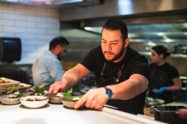 A chef places bowls of food on the pass of a restaurant kitchen.