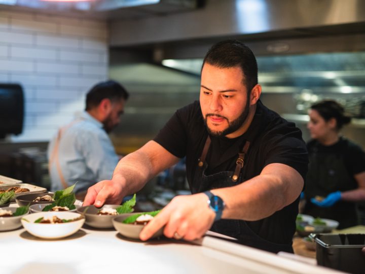 A chef places bowls of food on the pass of a restaurant kitchen.
