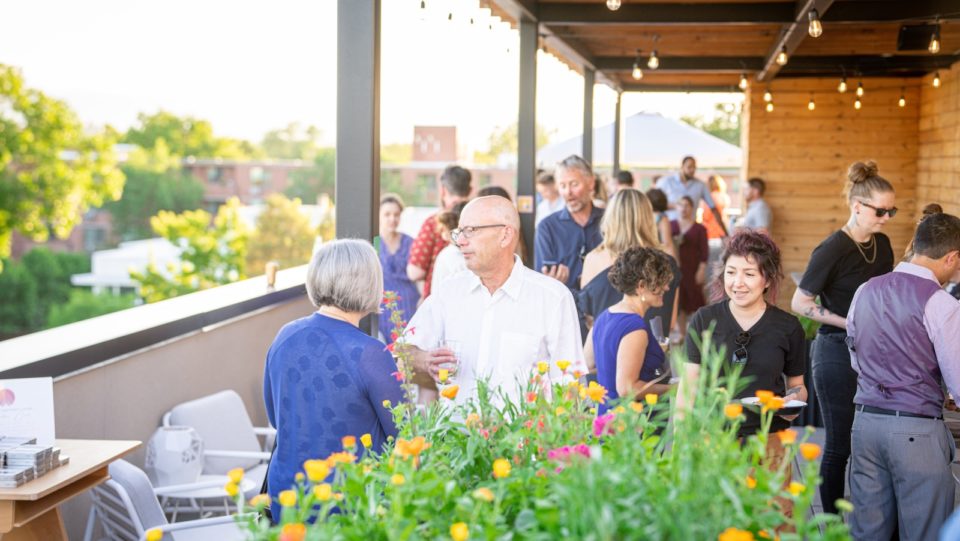 Restaurant customers hold drinks on a rooftop bar surrounded by flowers and treetops.