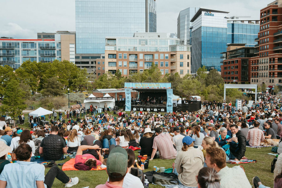 A crowd people in a park watching an outdoor concert.