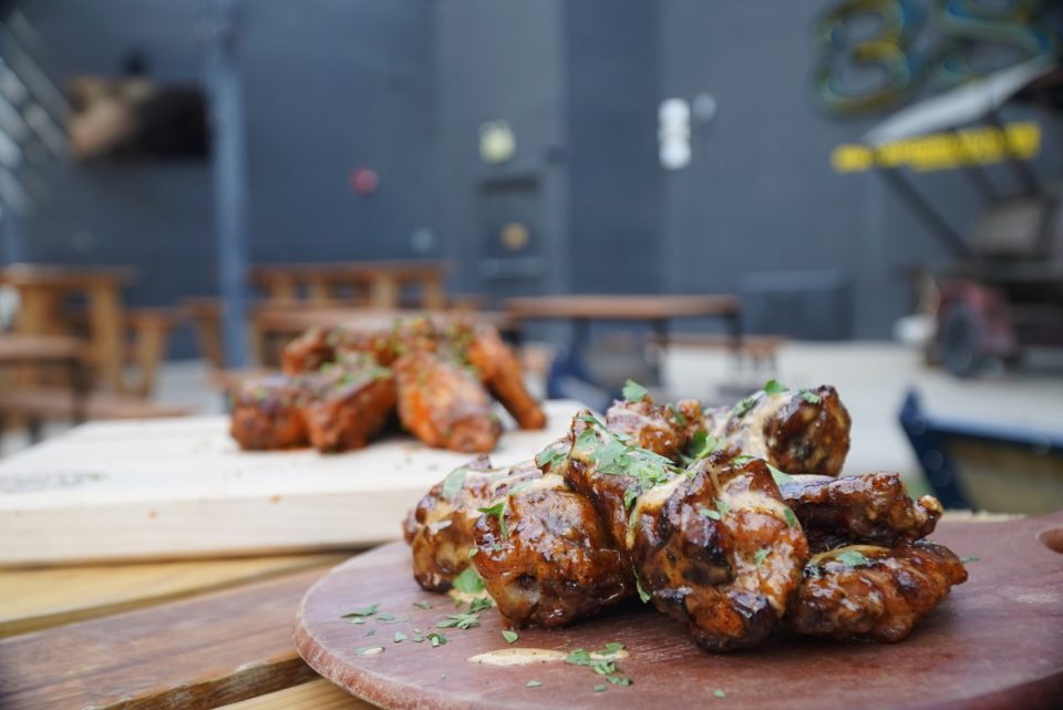A pile of chicken wings coated in sauce and fresh herbs on a round wooden board.