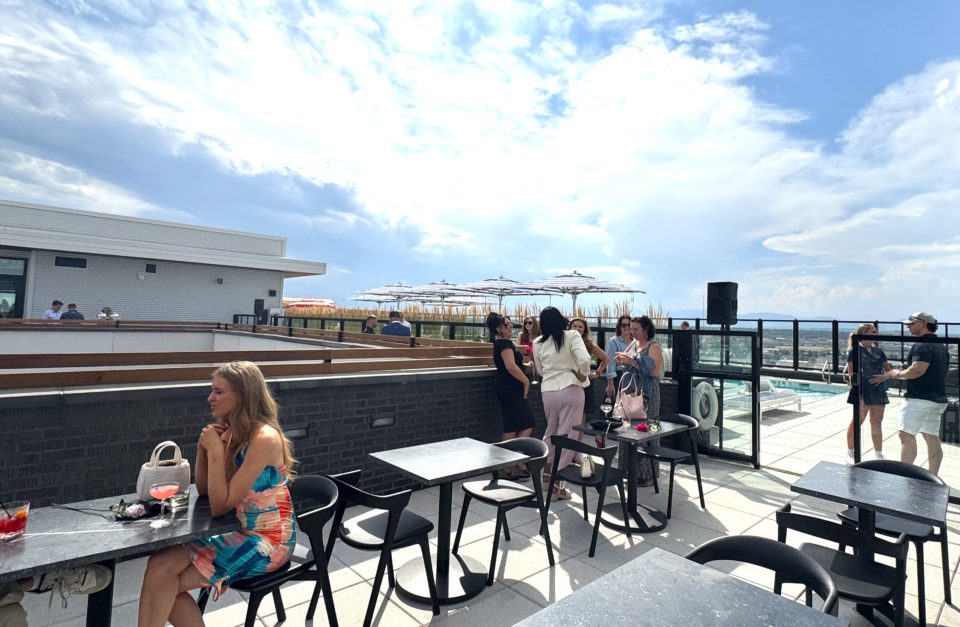 Seated and standing guests enjoy drinks at a rooftop bar and swimming pool.