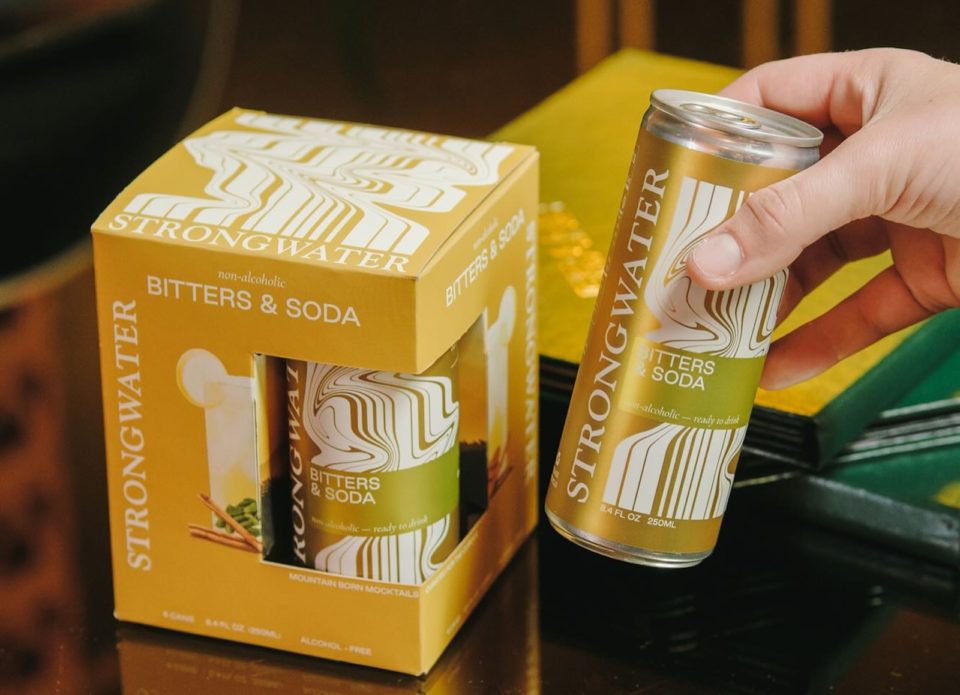 A box of Strongwater Bitters and Soda mocktails with a hand holding a can