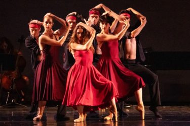 A group of dancers in red ballet outfits strike a pose on stage