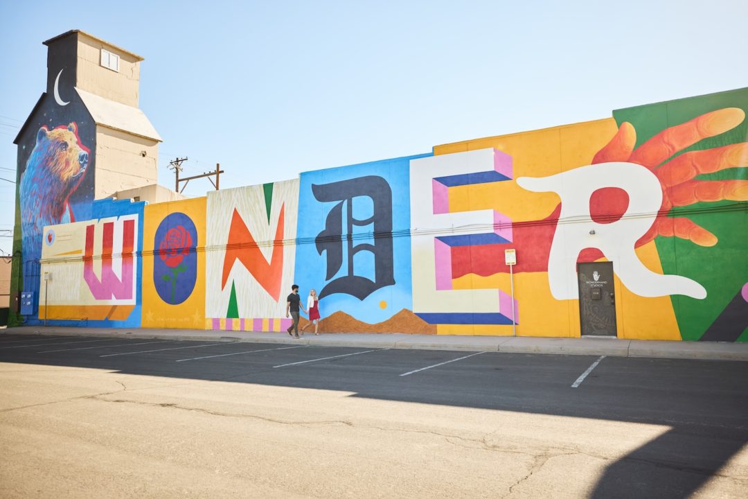 Two people hold hands walking by "Wonder Mural" by Armando Silva in Downtown Greeley