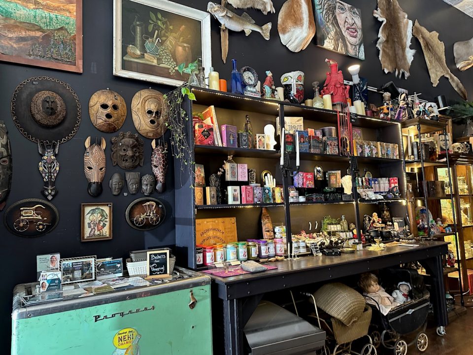 Shelves at the Downtown Oddities Parlor displaying candles and tarot cards, masks and paintings line the walls