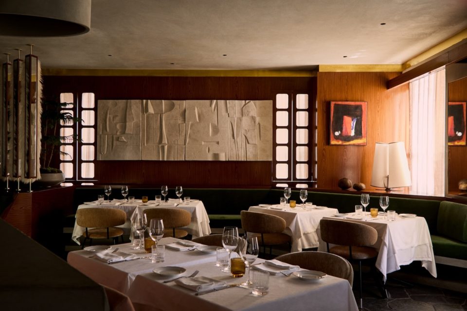 Dimly lit restaurant interior with textured midcentury modern art on one wall