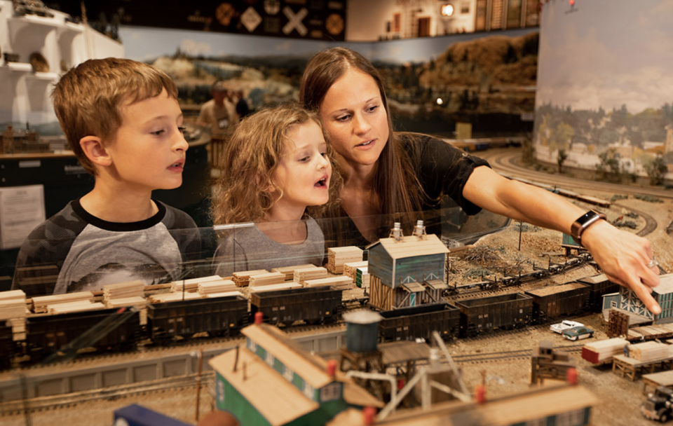 A woman and two children look at a model railroad track