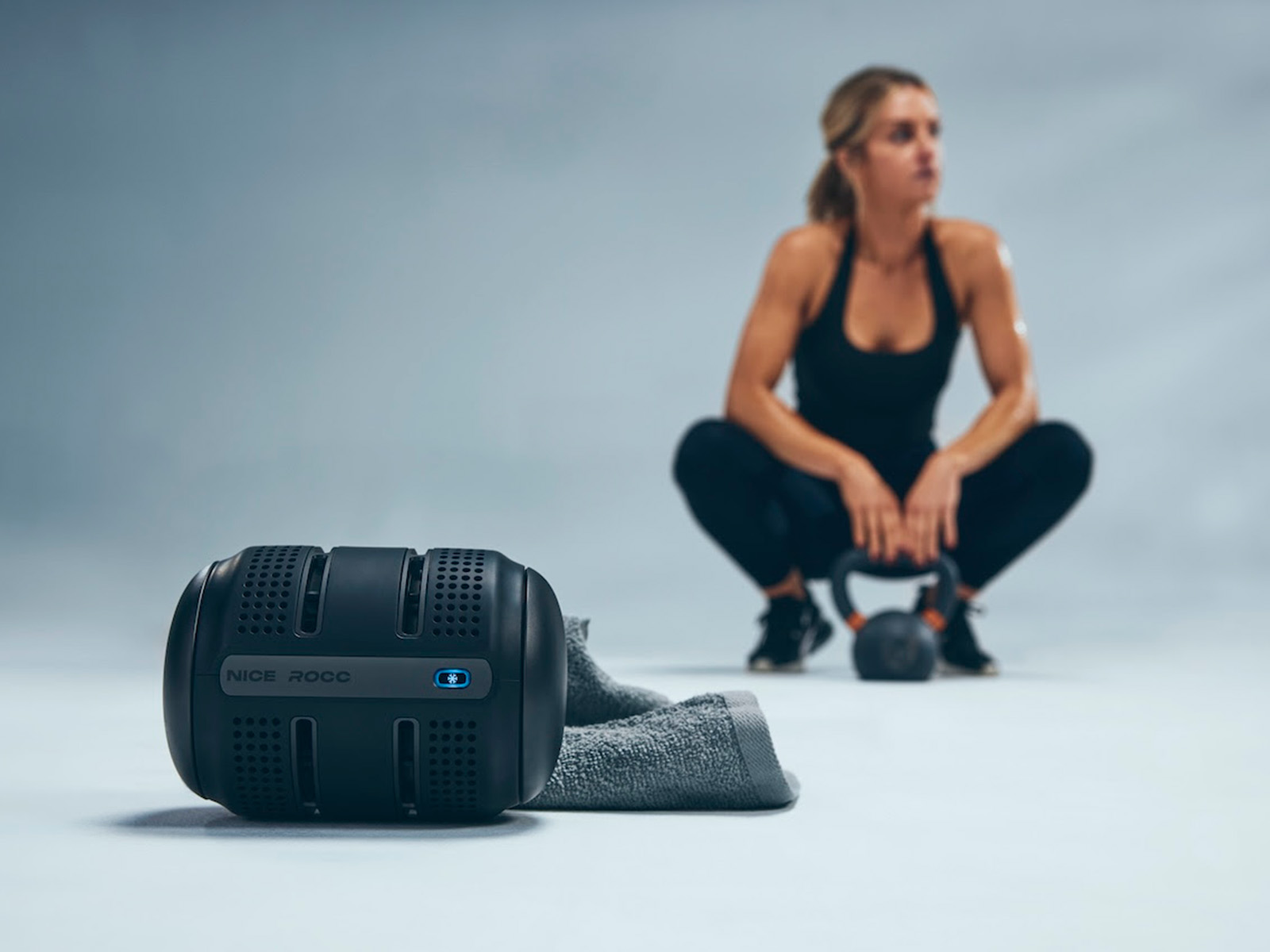 Woman squats behind a black device that looks like a bluetooth speaker