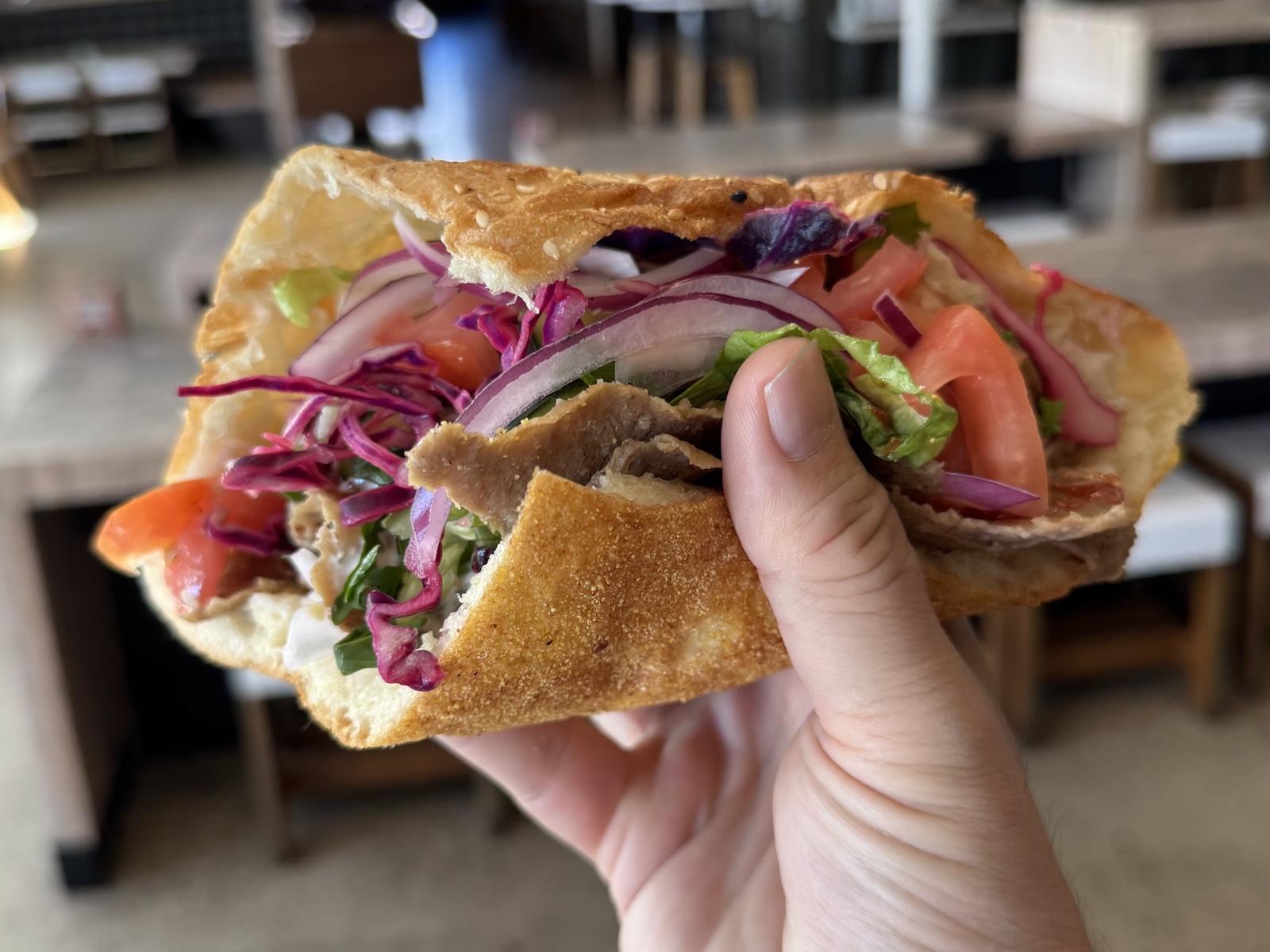 A hand holding a pita sandwich filled with shaved meat and fresh vegetables