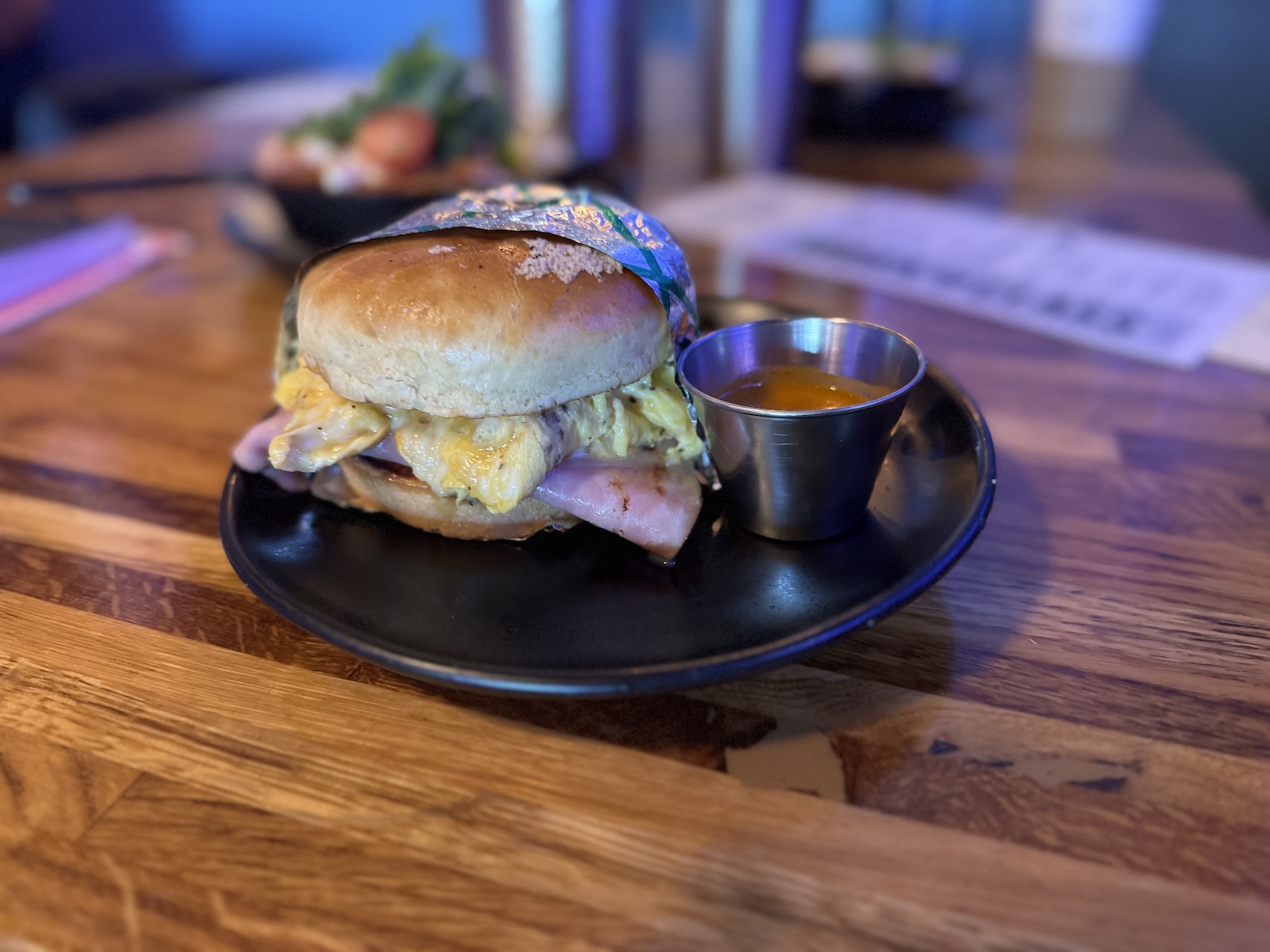 A breakfast sandwich with ham and scrambled eggs and a side of salsa