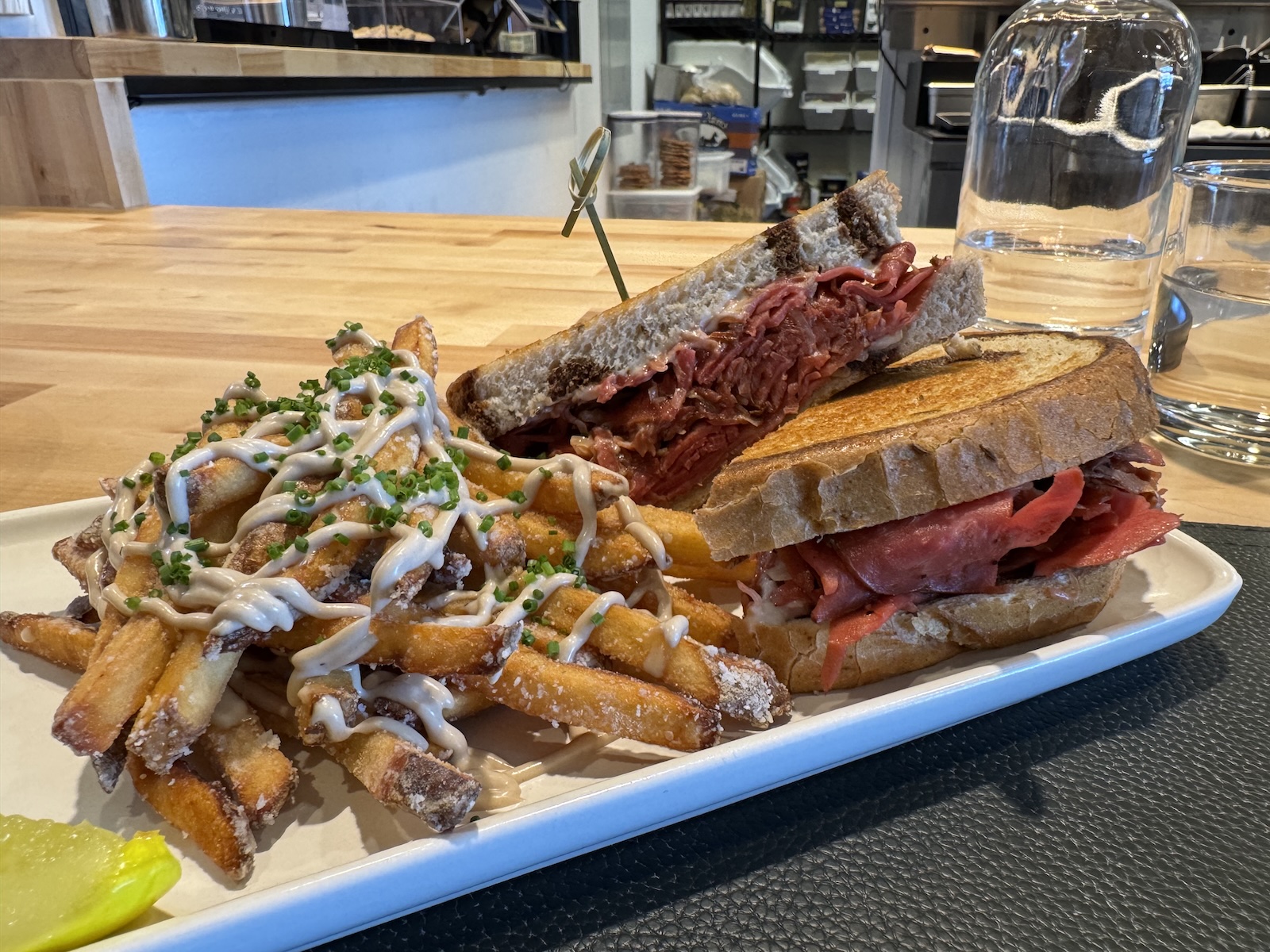 A reuben sandiwch with sauce-covered fries on a rectangular plate