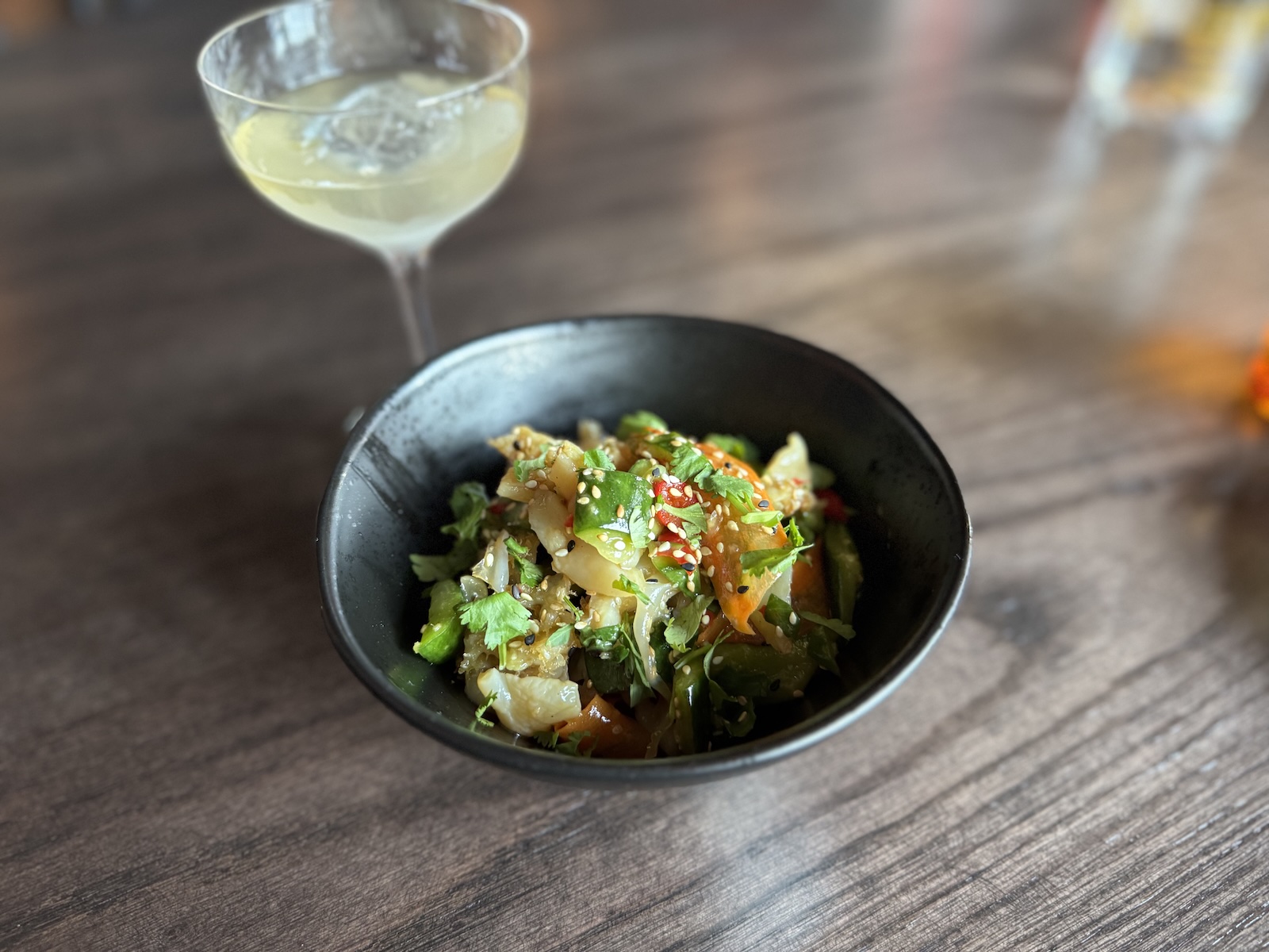 A salad in a black bowl with a stemmed cocktail glass.