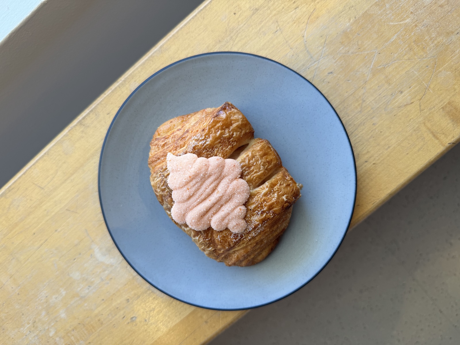 A croissant topped with pink frosting on a blue plate