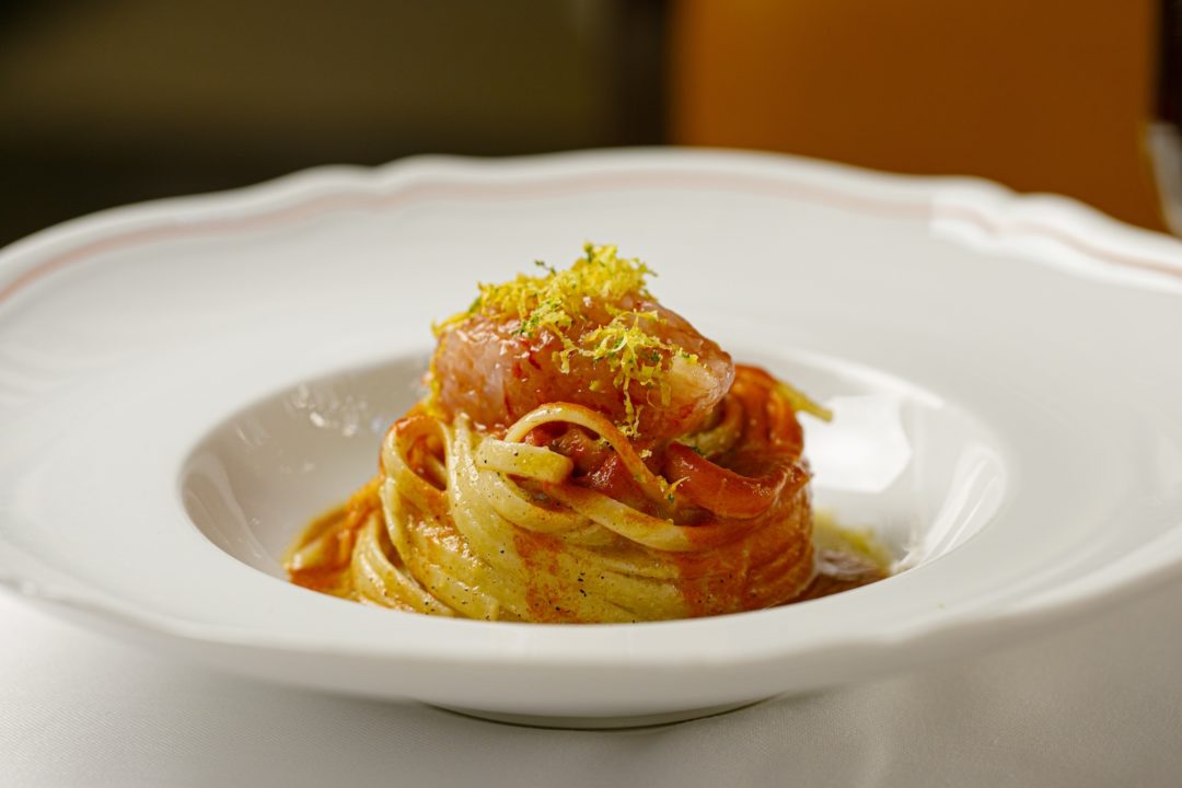 A twirled mound of fettuccini with tomao sauce and a piece of rare fish.