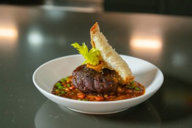 Venison osso bucco with a slice of bread in a white bowl