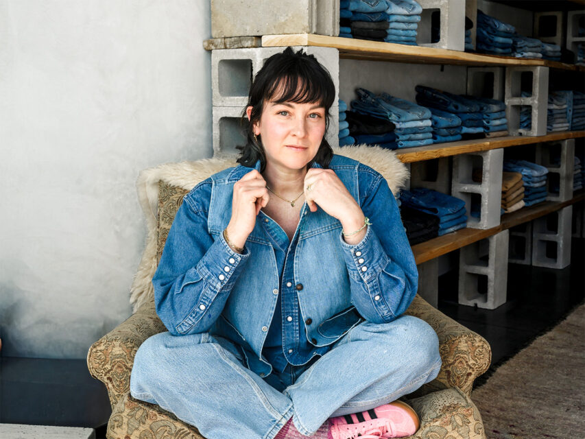 Woman wearing all denim sits cross-legged in a chair