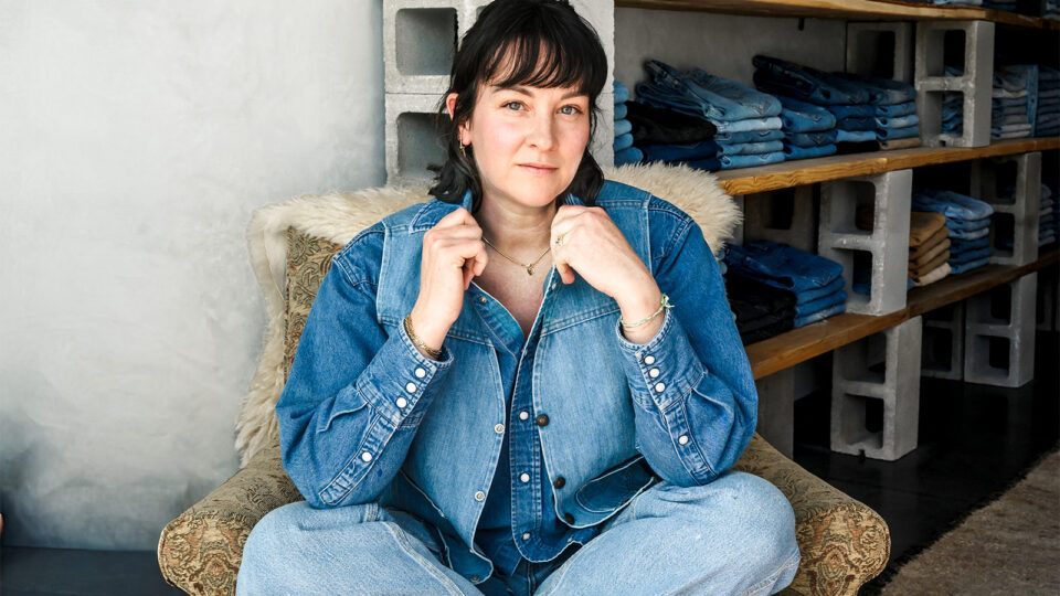 Woman wearing all denim sits cross-legged in a chair