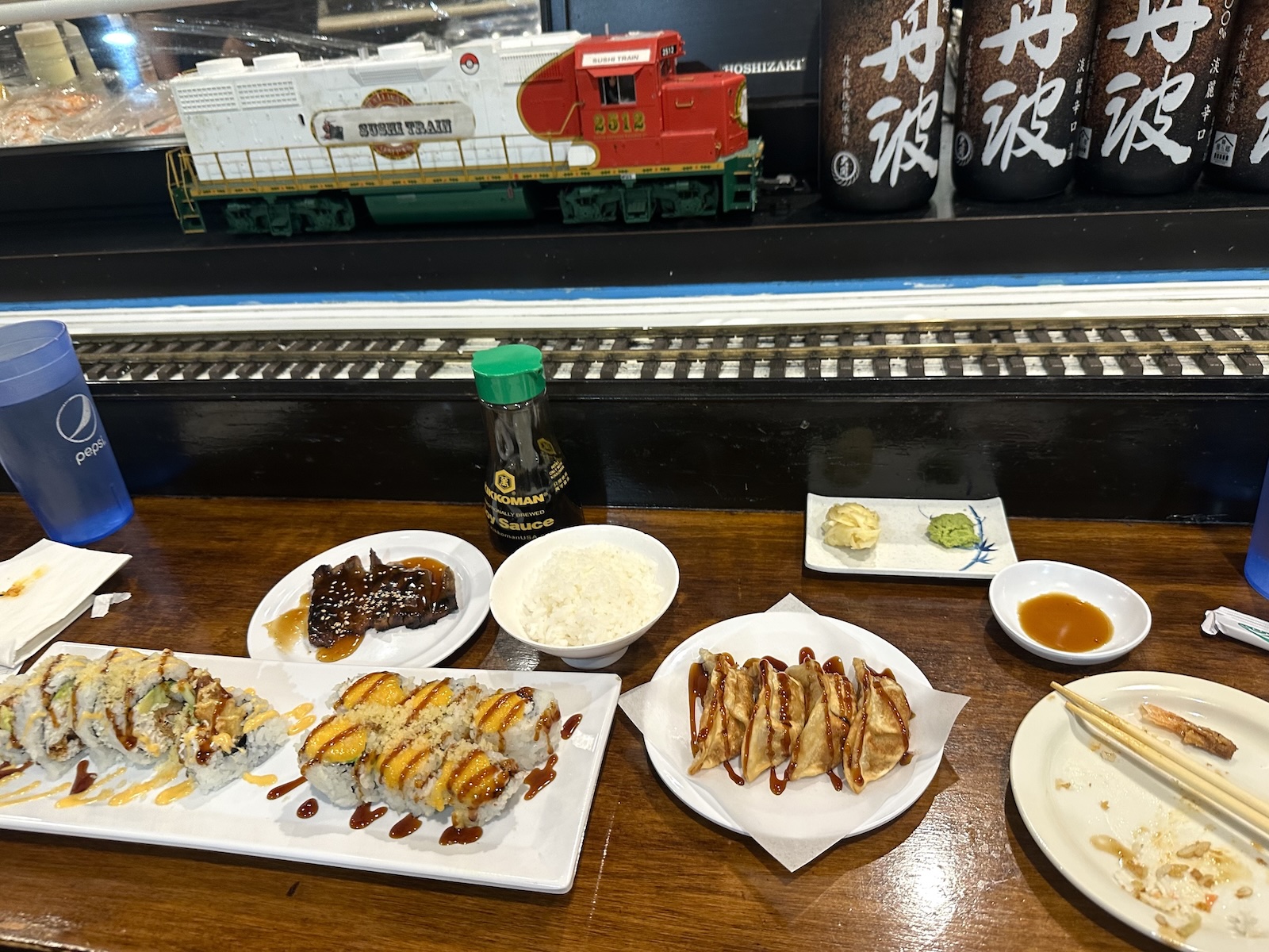 Several plates of sushi, rices, sauces, and side dishes at a sushi bar with miniature train track