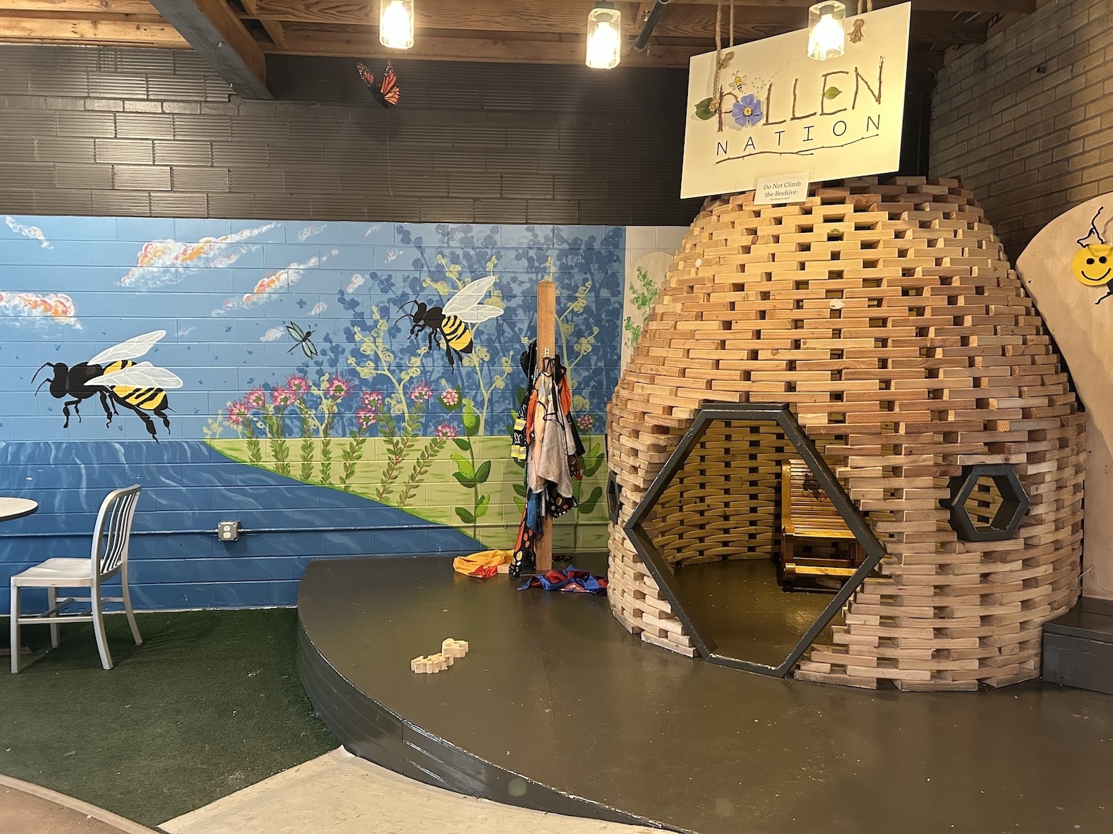 A giant wooden beehive labeled "pollen nation" next to a mural depicting bees inside a restaurant