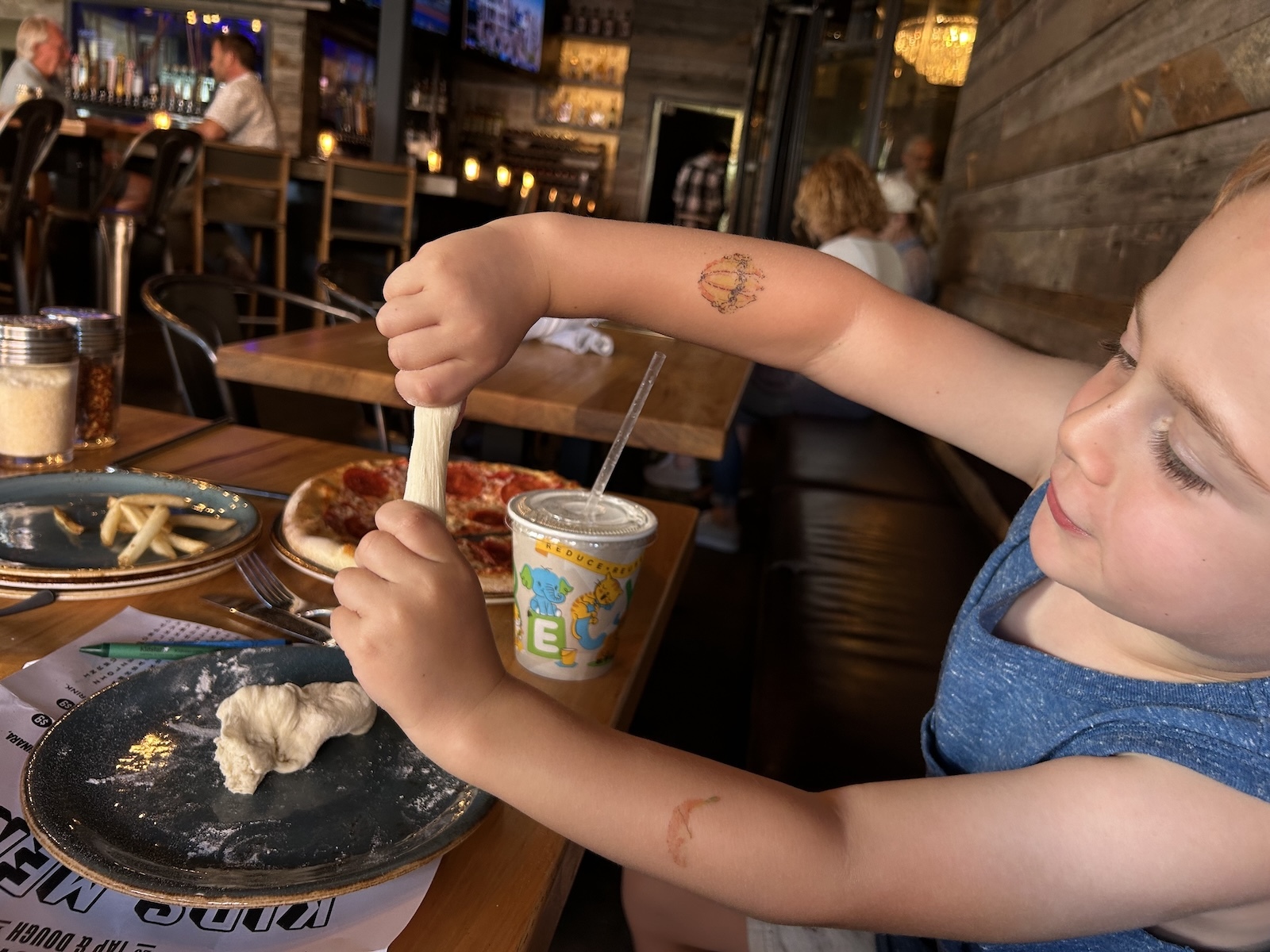 A child playing with dough while sitting at a restaurant table with a mini pizza