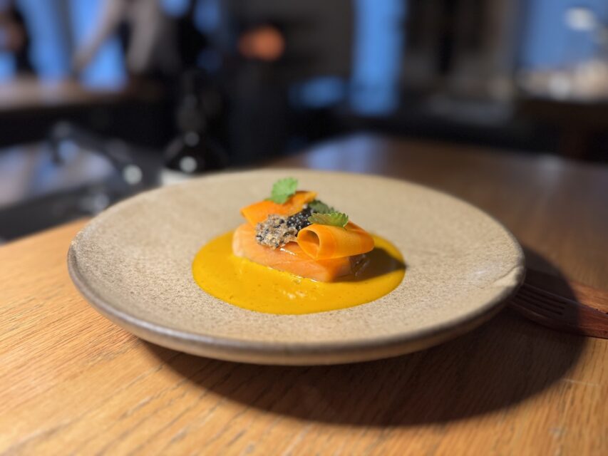 Stoneware plate holding a salmon fillet in orange sauce topped with a curl of carrot
