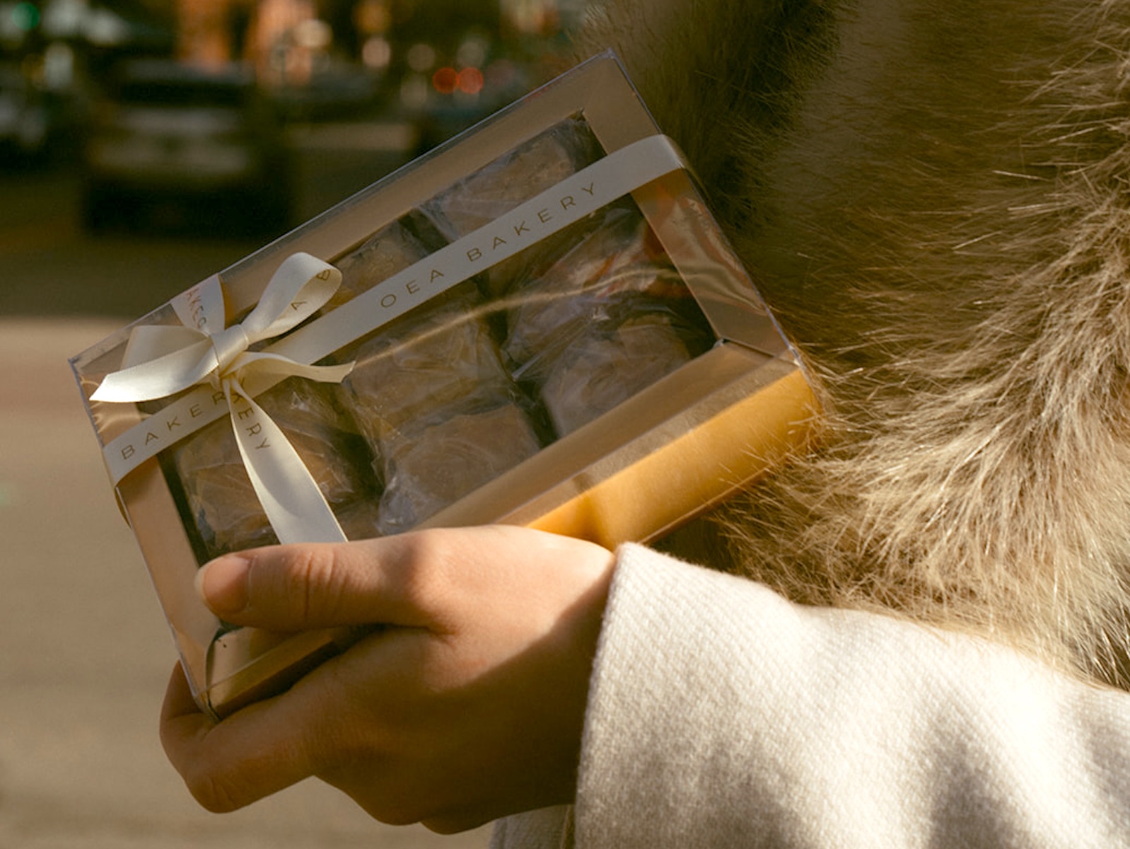 A gift box with a white ribbon labeled Oea Bakery holding baklava.