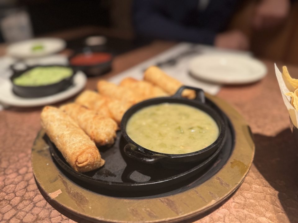 A cast iron skillet holding green chile stew with crispy chily rellenos, all on a round wooden board.
