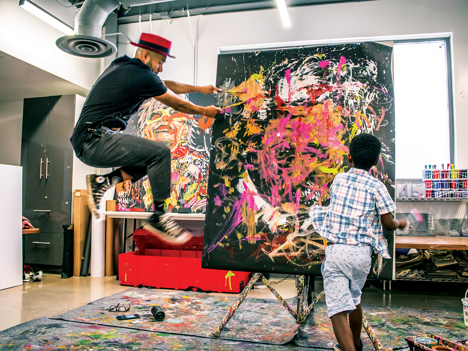 A man and a young boy throwing paint on a canvas