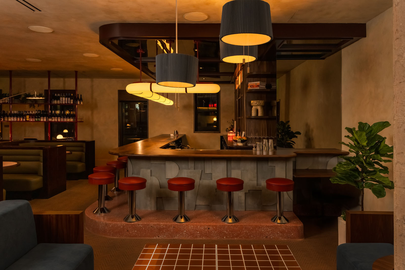 L-shaped bar with red barstools atop a terrazzo platform
