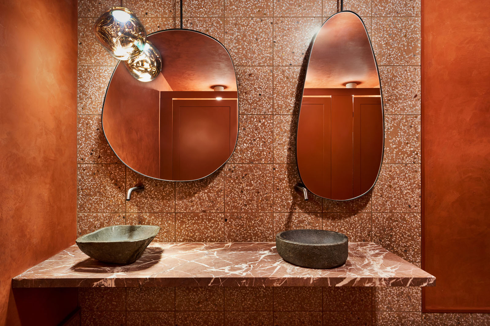 Funky shaped mirrors over a marble countertop and stone sinks in the bathroom