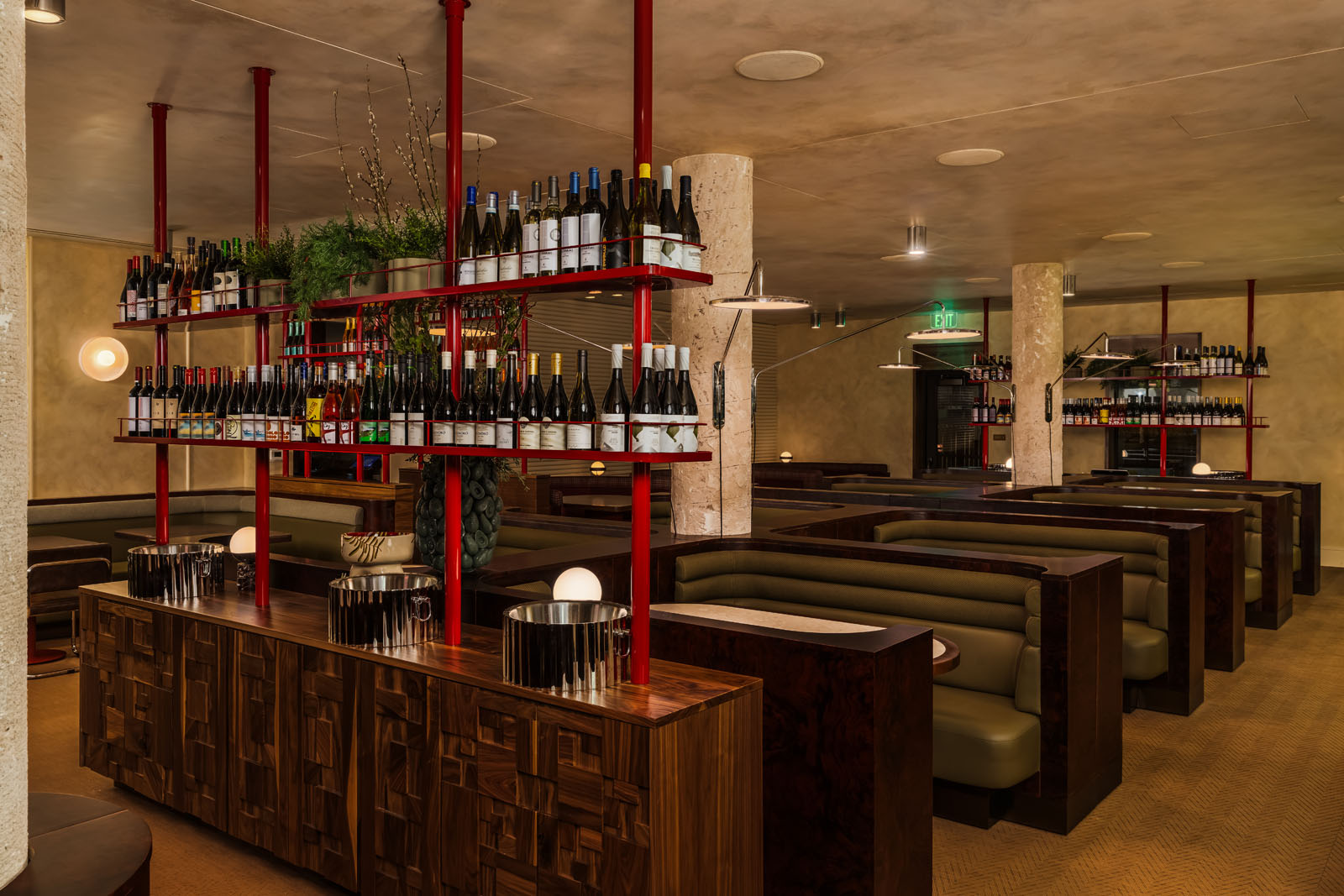 Red-lacquered shelving holds wine bottles beside forest green booths