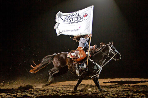 A woman riding a horse holding a flag that says National Western Stock Show.