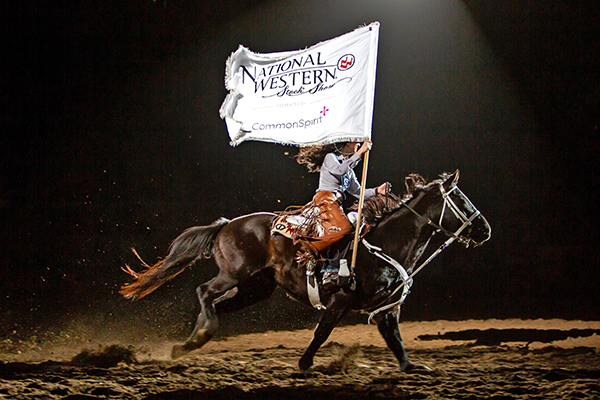 A woman riding a horse holding a flag that says National Western Stock Show.