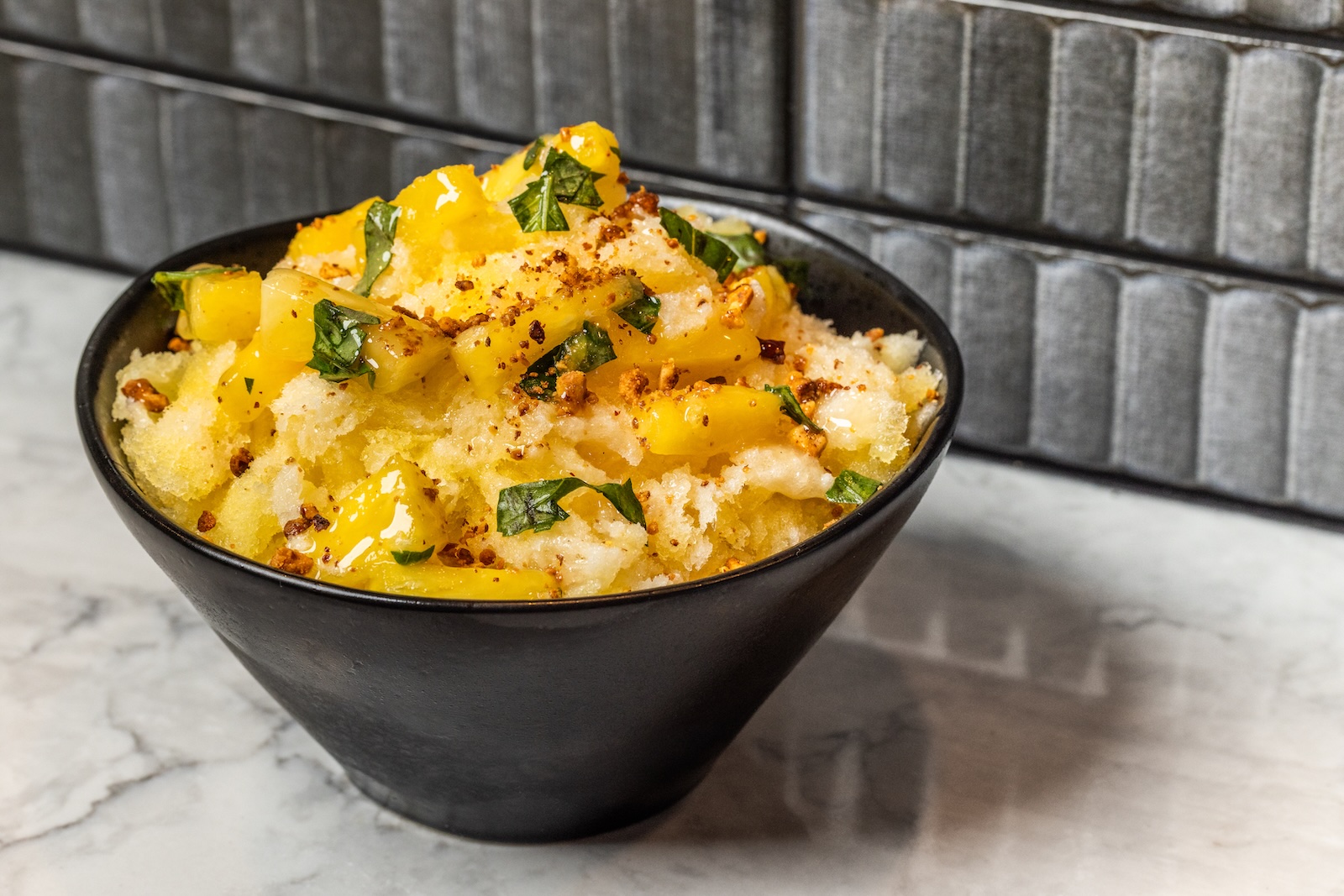 A black bowl filled with pineapple shaved ice and topped with diced pineapple