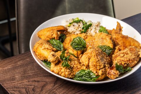 A while bowl with eight pieces of fried chicken, a small portion of rice, and fried basil leaf garnish