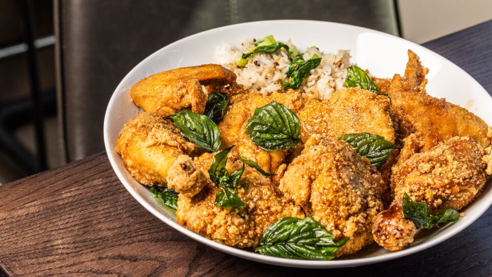 A while bowl with eight pieces of fried chicken, a small portion of rice, and fried basil leaf garnish