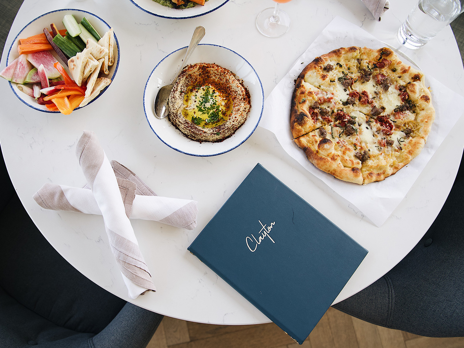Table with a Clayton menu, pizza, and hummus