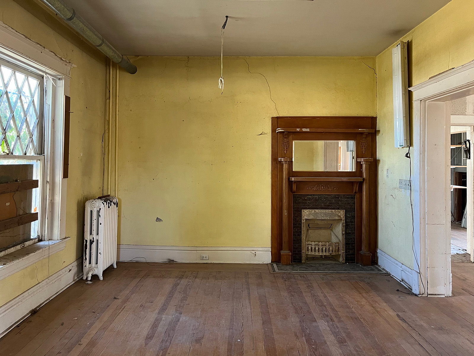 Empty dining room with an old wooden fireplace and peeling wallpaper