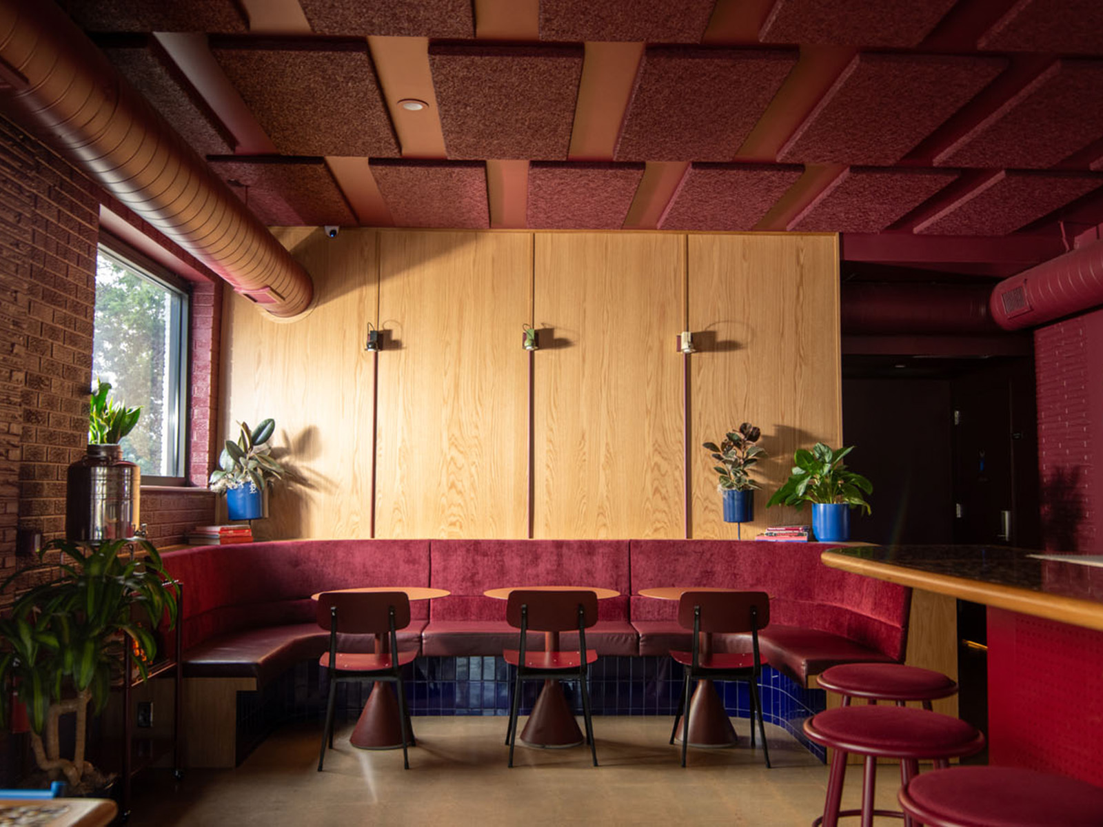 Red velvet banquette against a light wood wall with red metal chairs
