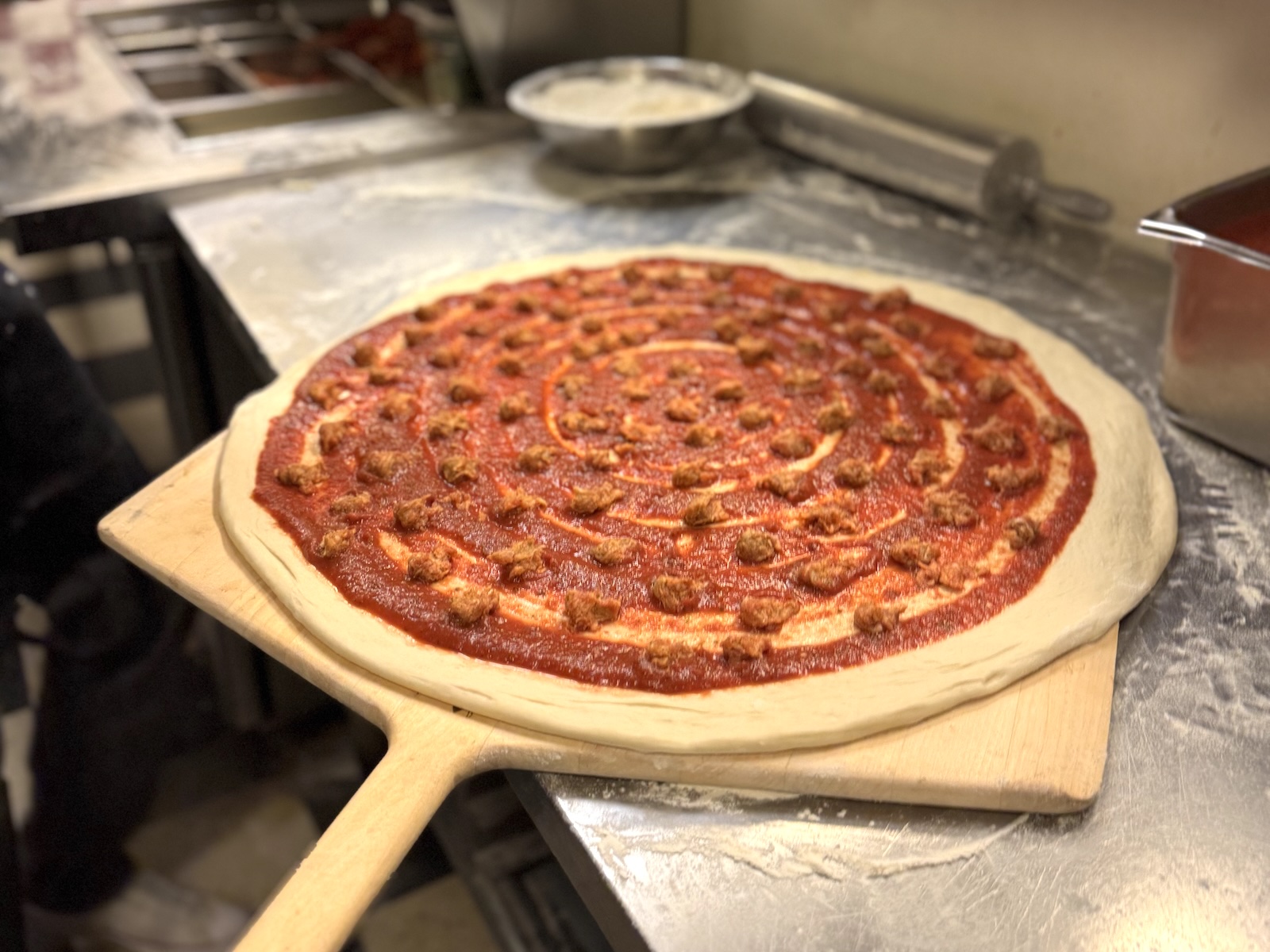 An uncooked pizza on a wooden peel with sauce and sausage but no cheese