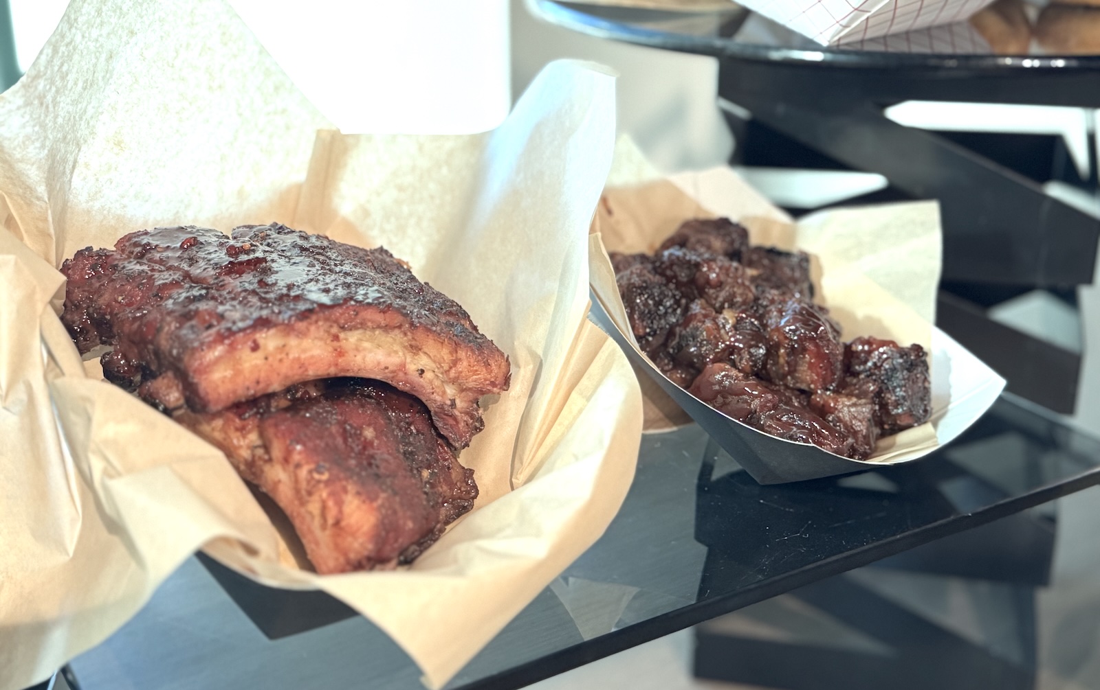 Barbecue pork ribs in a paper-lined basket on the left and glazed brisket burnt ends on the right.