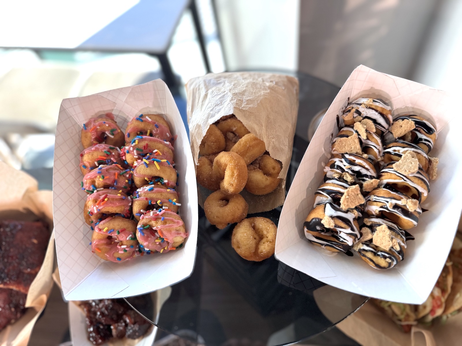 Two paper baskets and one paper bag filled with mini doughnuts